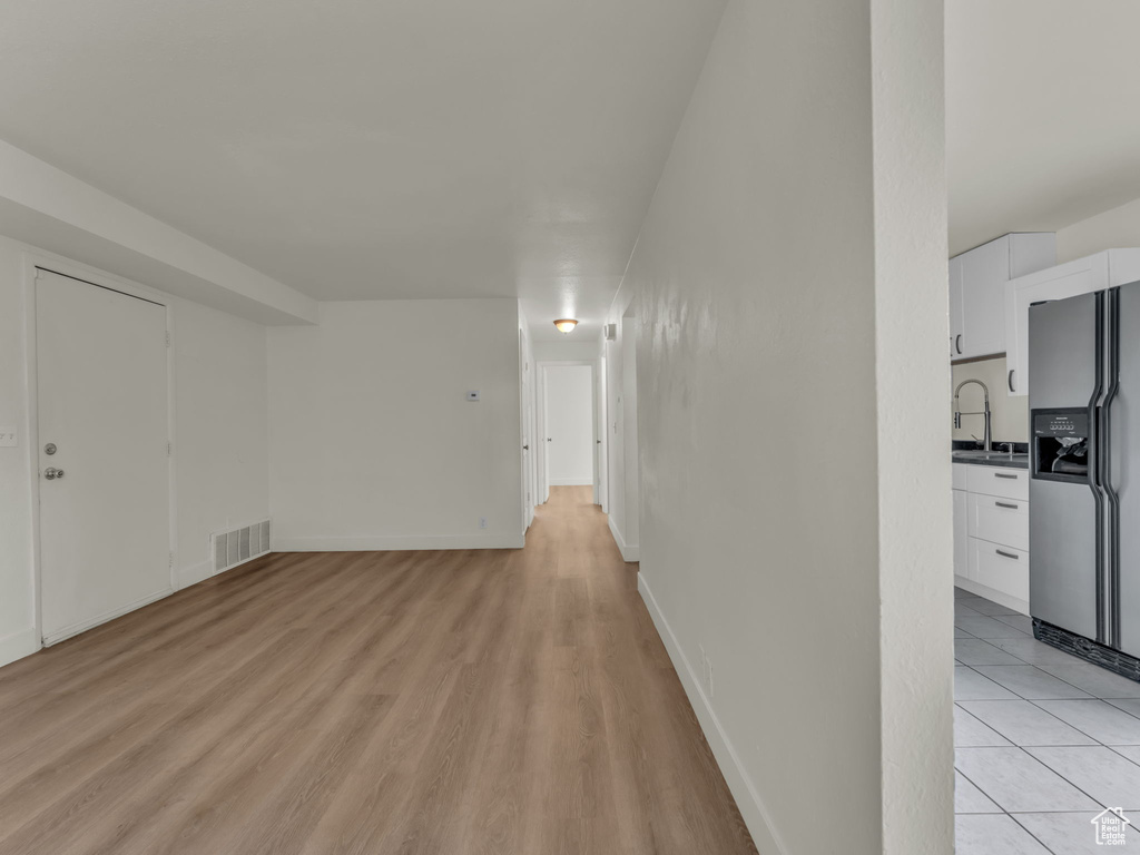 Unfurnished living room featuring a sink, light wood-style flooring, and baseboards