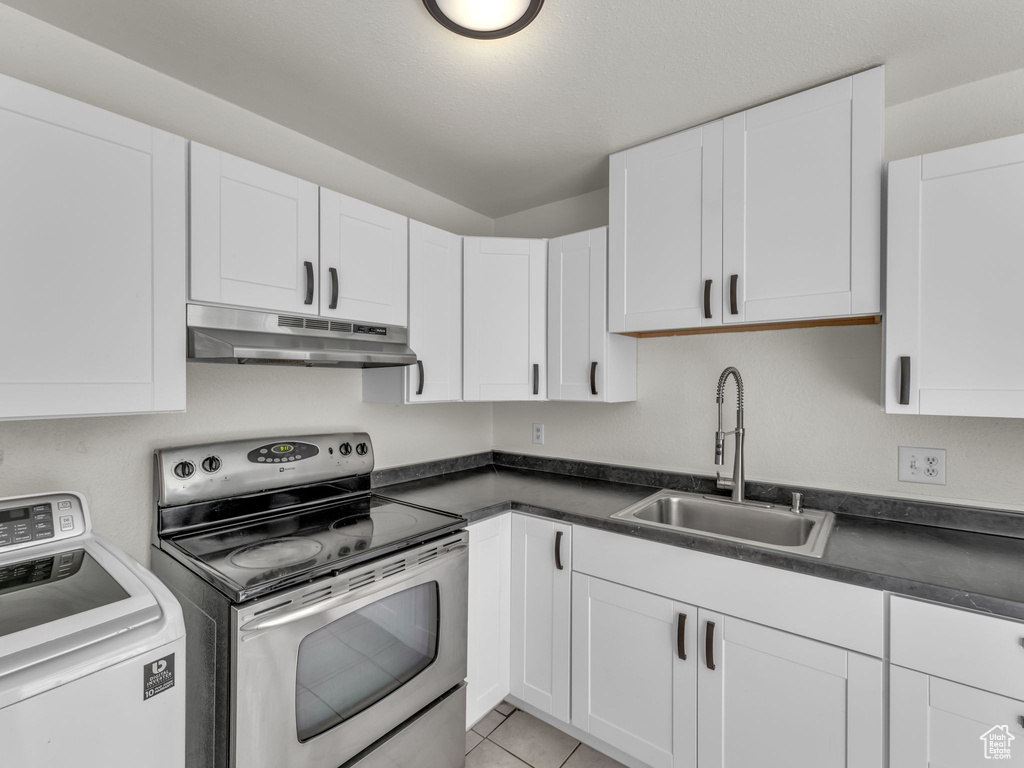 Kitchen featuring washer / clothes dryer, under cabinet range hood, stainless steel electric stove, a sink, and dark countertops