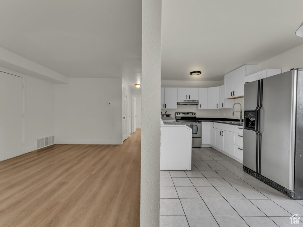 Kitchen featuring refrigerator with ice dispenser, stainless steel electric range, under cabinet range hood, white cabinets, and open floor plan
