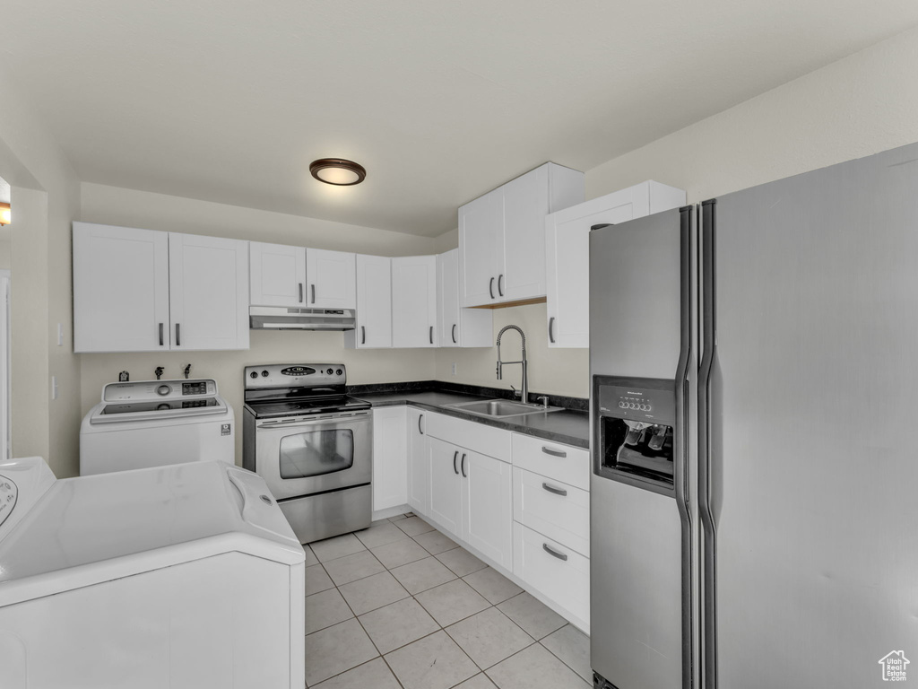 Kitchen with stainless steel appliances, a sink, under cabinet range hood, washer and dryer, and light tile patterned flooring