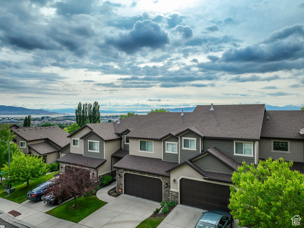 View of front facade with roof with shingles, an attached garage, driveway, a mountain view, and a residential view