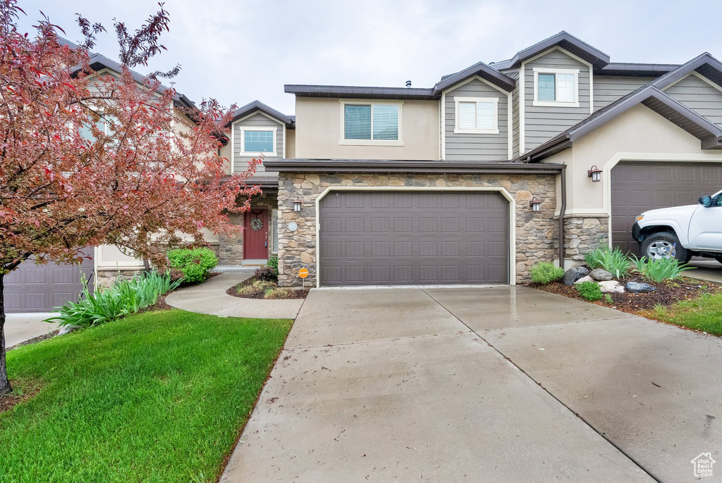 View of front of house with stone siding, stucco siding, driveway, and an attached garage