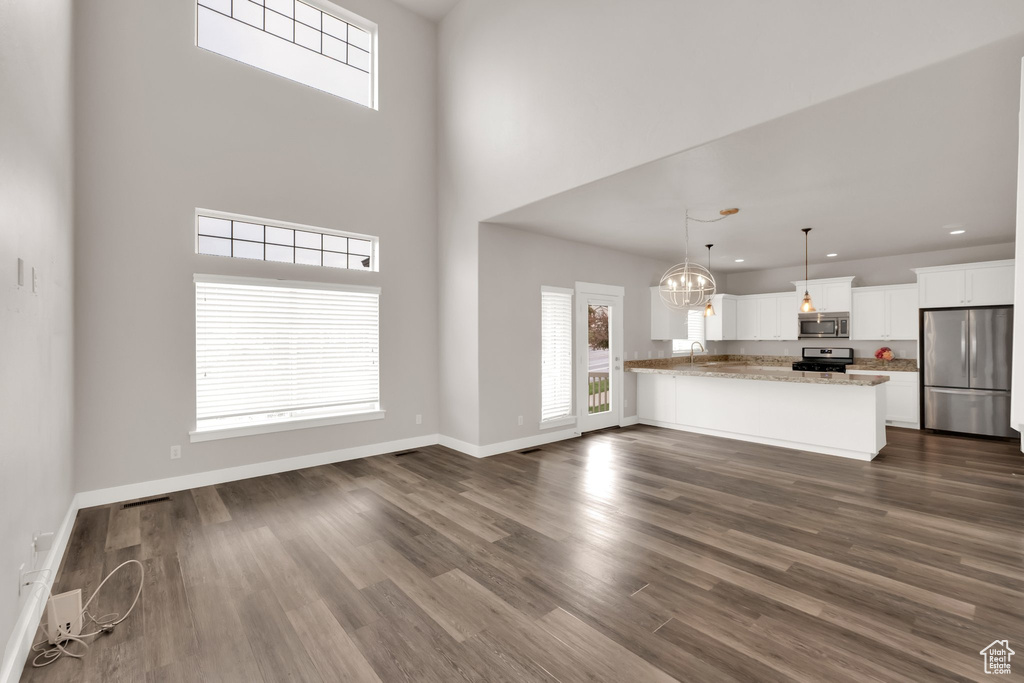 Unfurnished living room with dark wood-type flooring, a towering ceiling, recessed lighting, baseboards, and a chandelier