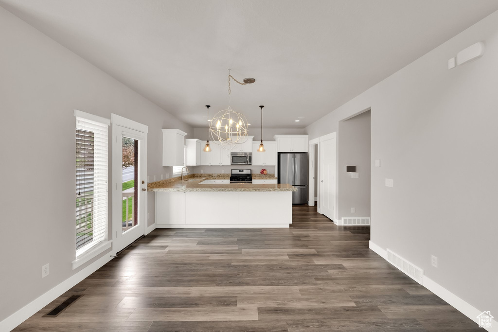 Kitchen featuring appliances with stainless steel finishes, a peninsula, a chandelier, white cabinets, and baseboards
