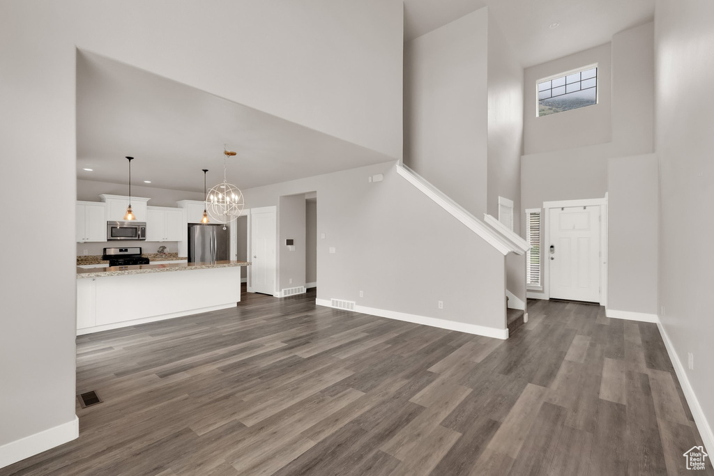 Unfurnished living room with a high ceiling, a chandelier, dark wood finished floors, baseboards, and stairs