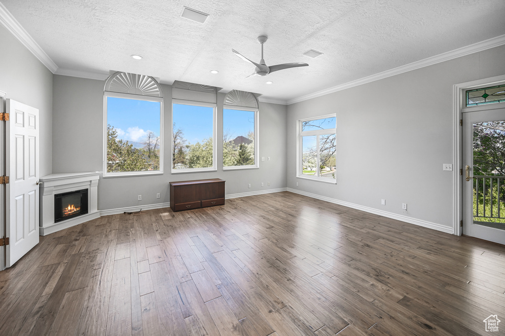 Unfurnished living room featuring a textured ceiling, crown molding, ceiling fan, and dark wood-style floors