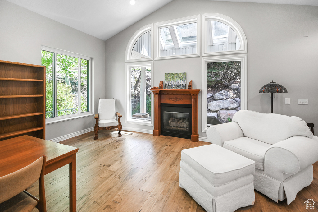 Sitting room featuring baseboards, high vaulted ceiling, a glass covered fireplace, and wood finished floors