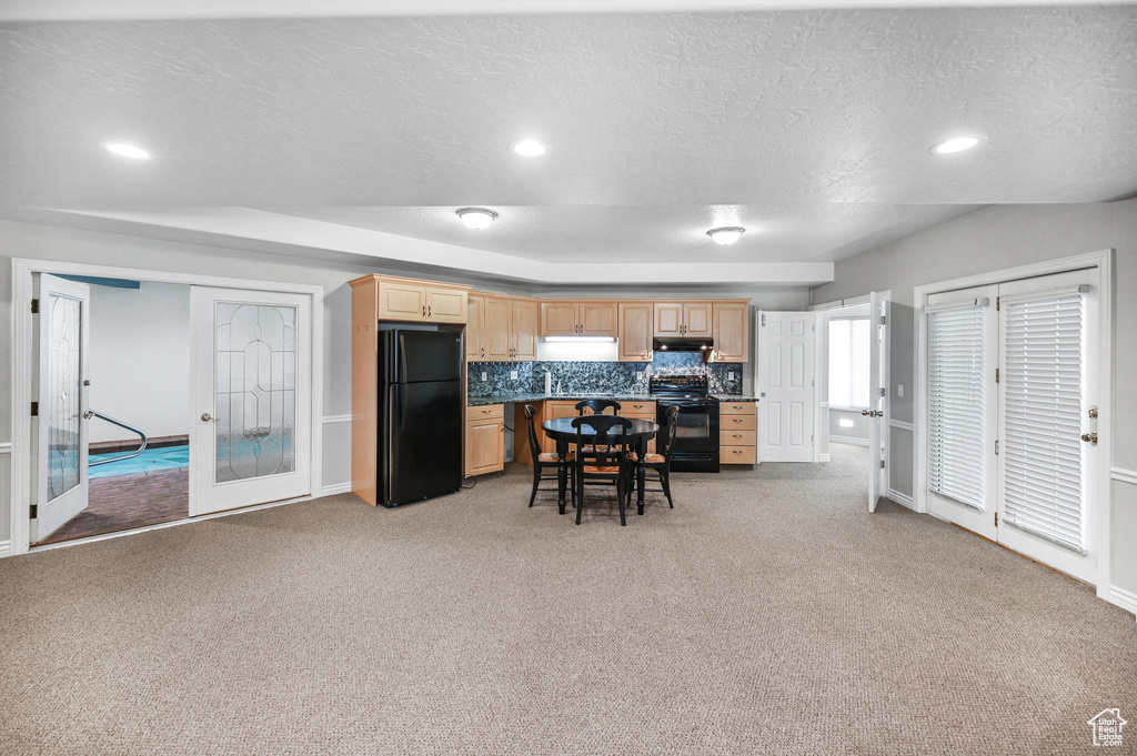 Kitchen featuring under cabinet range hood, light colored carpet, light brown cabinets, and black appliances