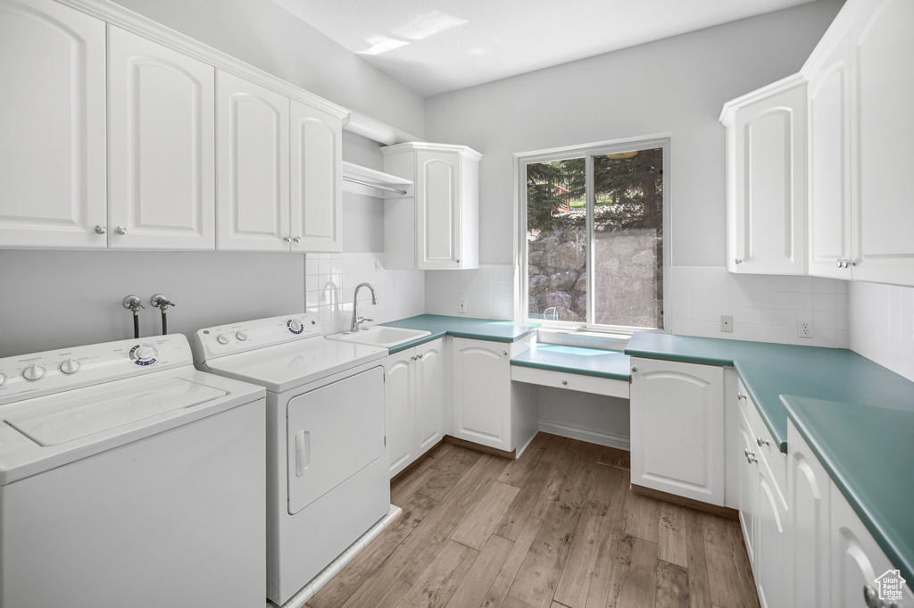 Laundry room with a sink, light wood-style flooring, cabinet space, and washer and dryer