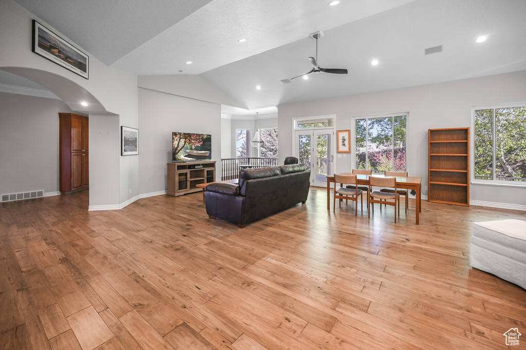 Living room with light wood-type flooring, visible vents, vaulted ceiling, arched walkways, and a ceiling fan