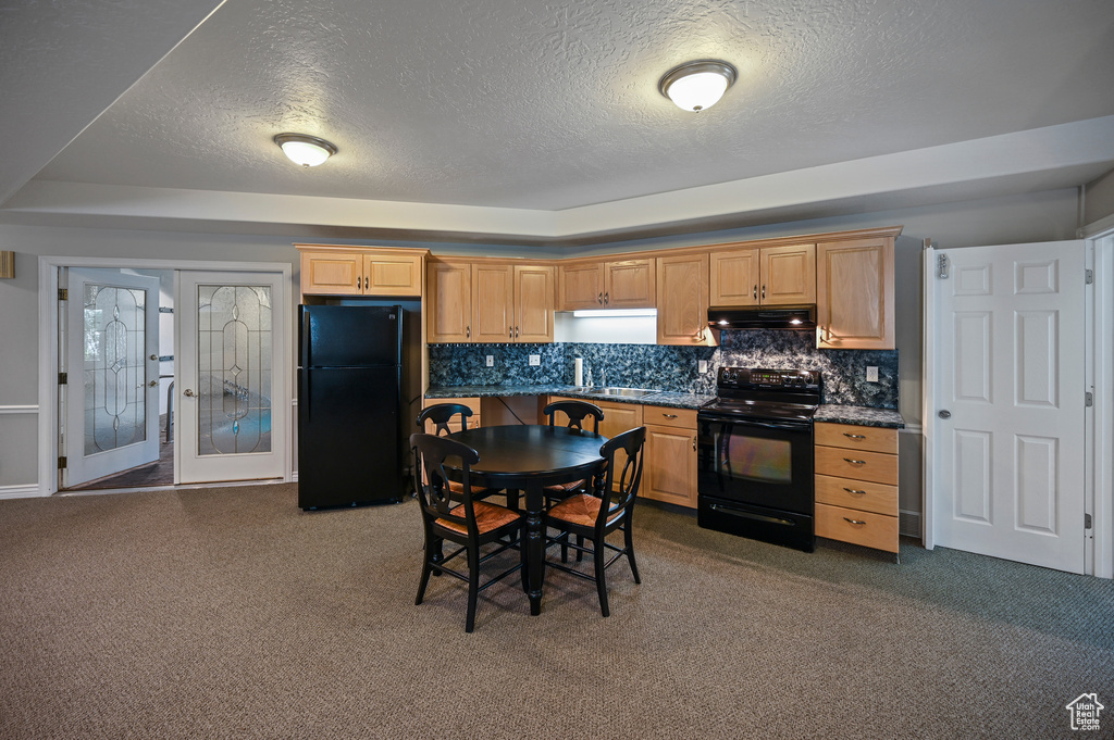Kitchen with a textured ceiling, black appliances, under cabinet range hood, dark colored carpet, and dark countertops