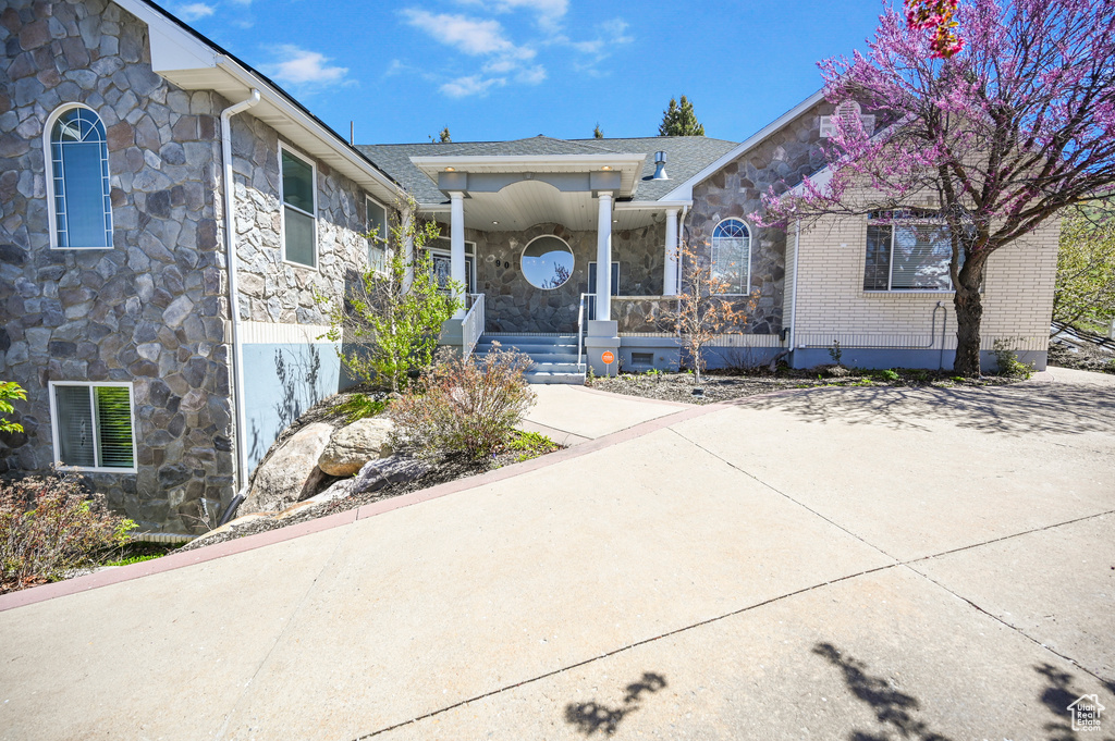 Property entrance with a porch, roof with shingles, stone siding, and visible vents