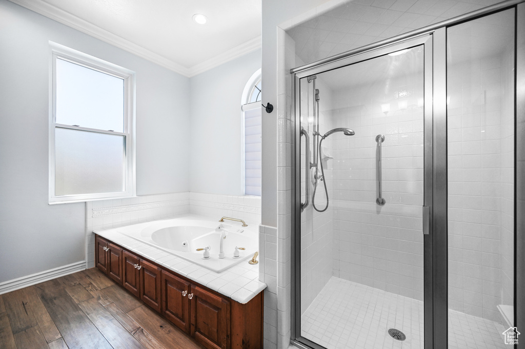 Full bathroom with a wealth of natural light, ornamental molding, a whirlpool tub, and wood finished floors