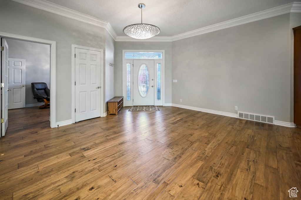 Foyer entrance with crown molding, wood-type flooring, and visible vents