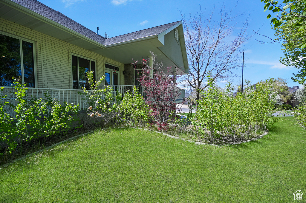 View of side of home featuring a shingled roof, brick siding, and a lawn