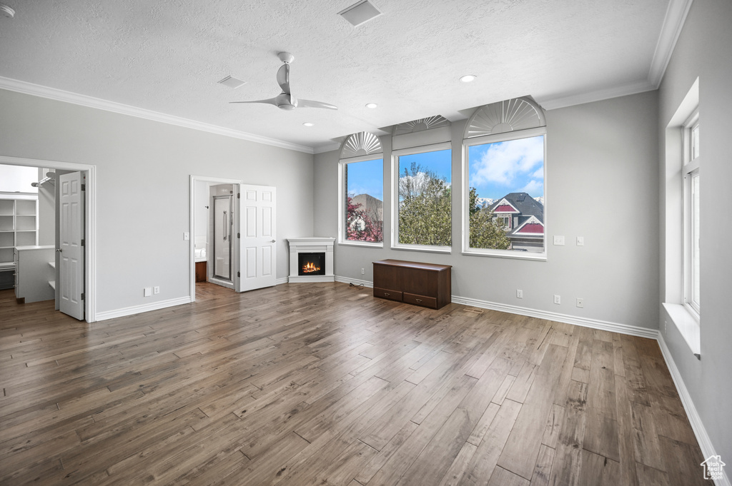 Unfurnished living room featuring a lit fireplace, ceiling fan, crown molding, and wood finished floors