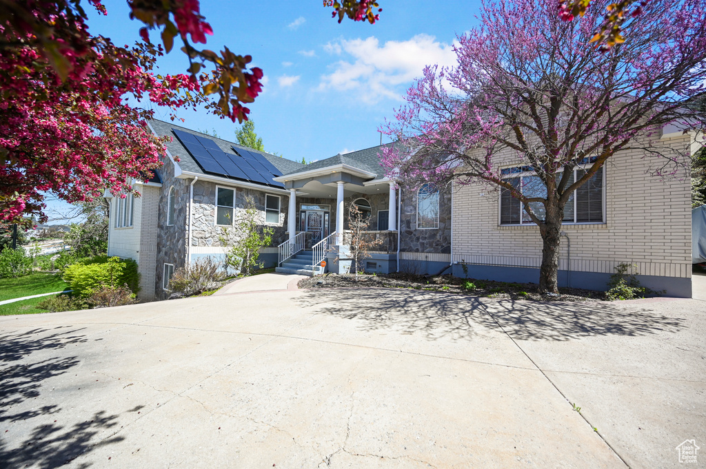 View of front facade featuring covered porch, roof mounted solar panels, brick siding, and stone siding