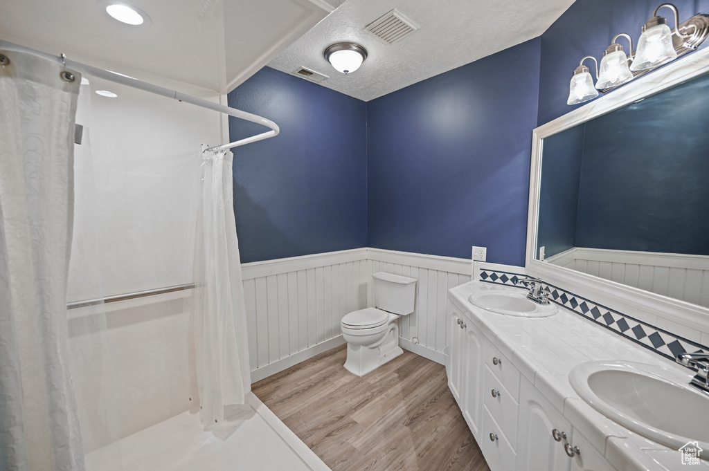 Full bath with a wainscoted wall, toilet, wood finished floors, and a sink