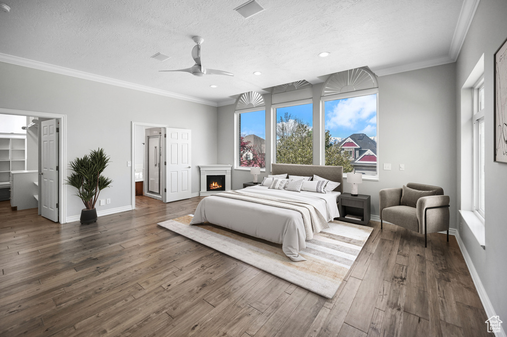 Bedroom featuring a textured ceiling, baseboards, ornamental molding, dark wood finished floors, and a lit fireplace