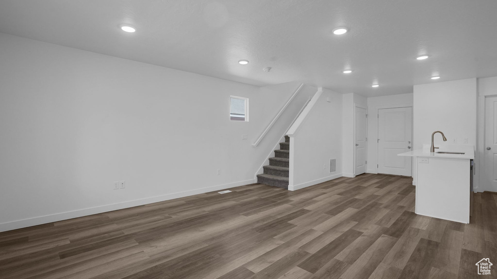 Unfurnished living room featuring a sink, stairs, dark wood-style flooring, recessed lighting, and baseboards
