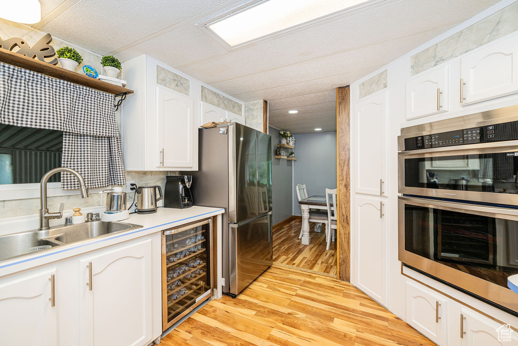 Kitchen featuring wine cooler, stainless steel appliances, a sink, white cabinets, and light wood-style floors