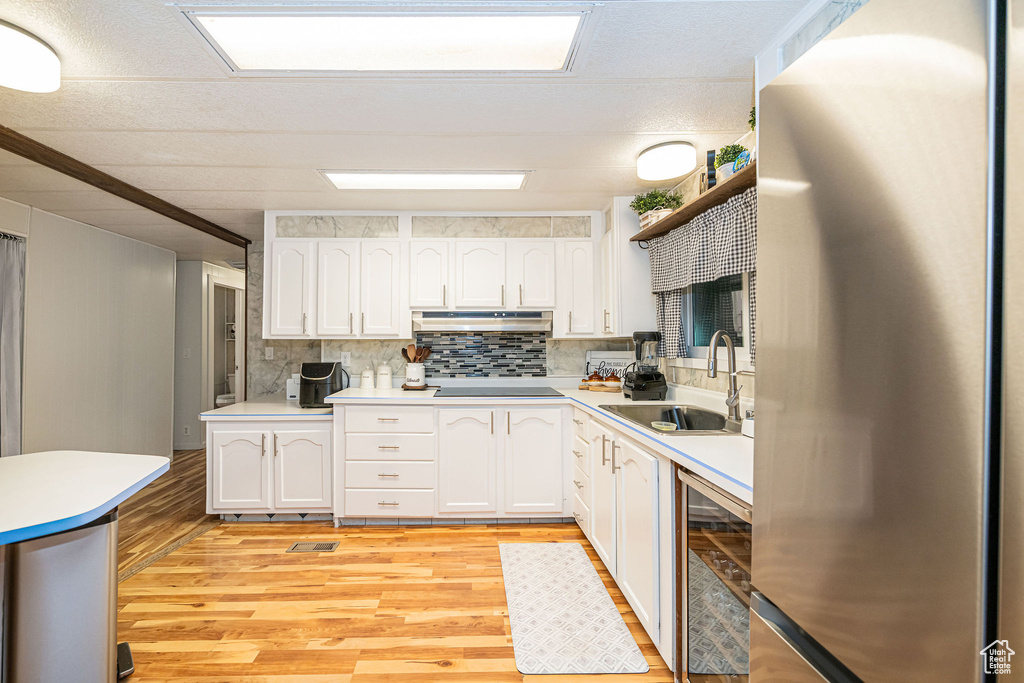 Kitchen featuring freestanding refrigerator, a sink, beverage cooler, white cabinets, and light wood-style flooring