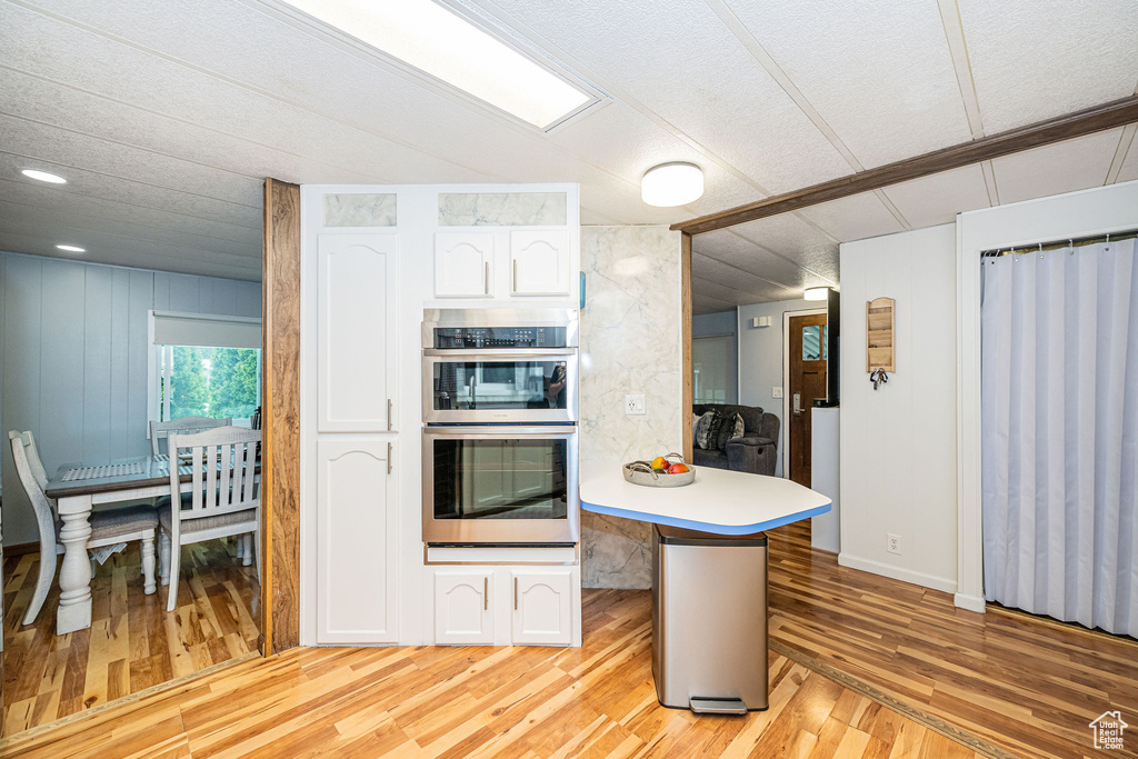Kitchen featuring light wood-type flooring, stainless steel double oven, a peninsula, and white cabinets