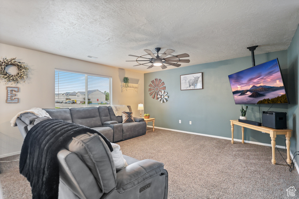 Carpeted living area with a textured ceiling, ceiling fan, and baseboards