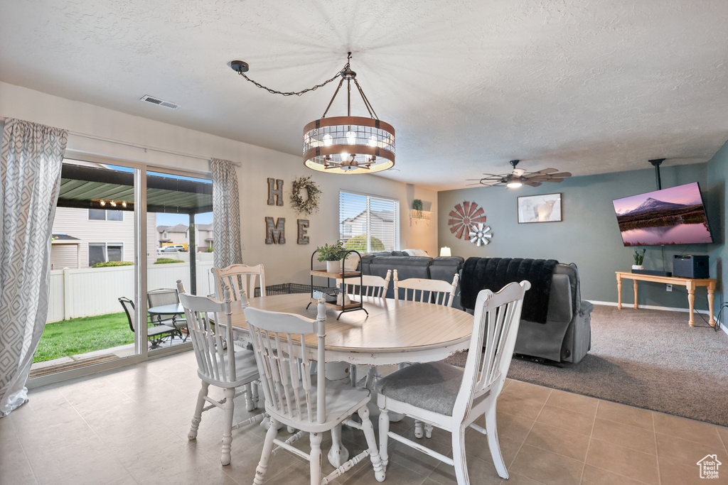 Dining room featuring ceiling fan, a textured ceiling, a chandelier, baseboards, and light tile patterned flooring