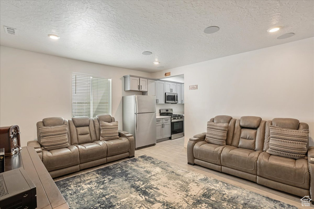 Living area featuring light wood-style floors, a textured ceiling, and recessed lighting
