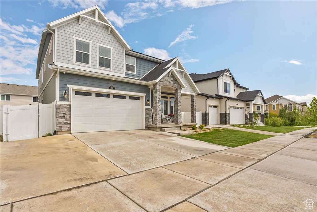 Craftsman-style house featuring stone siding, an attached garage, concrete driveway, a residential view, and fence