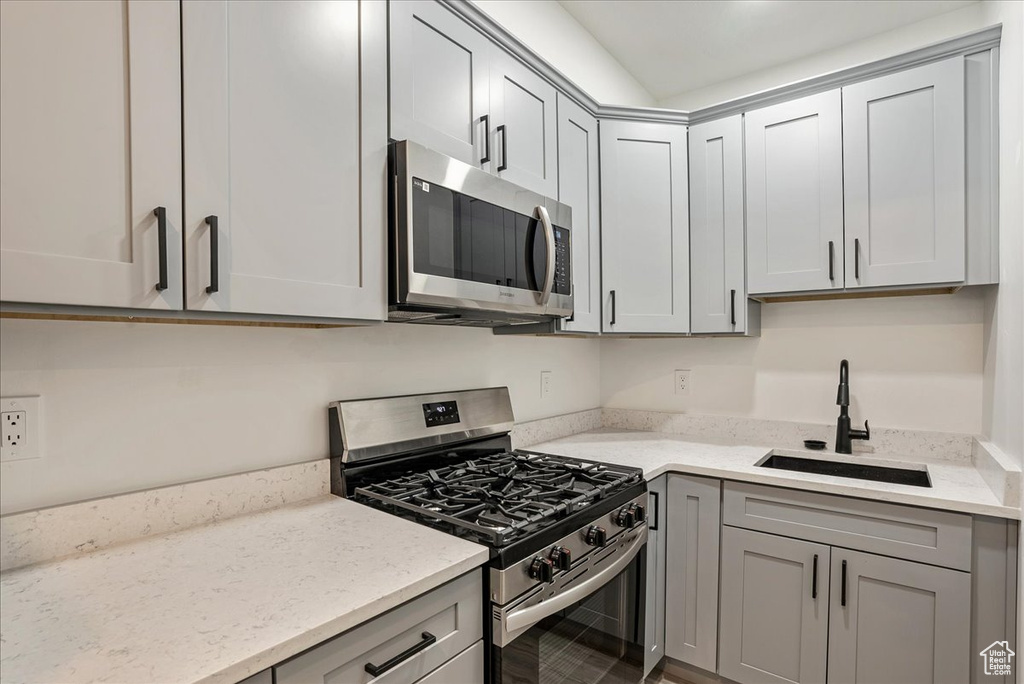 Kitchen with appliances with stainless steel finishes, a sink, gray cabinetry, and light stone counters
