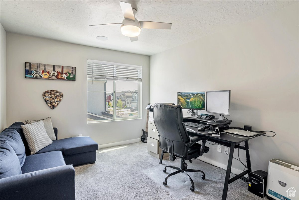 Carpeted office space with a textured ceiling, baseboards, and ceiling fan