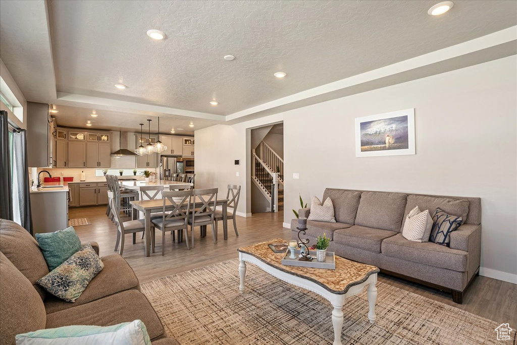 Living area with baseboards, stairs, a raised ceiling, a textured ceiling, and light wood finished floors