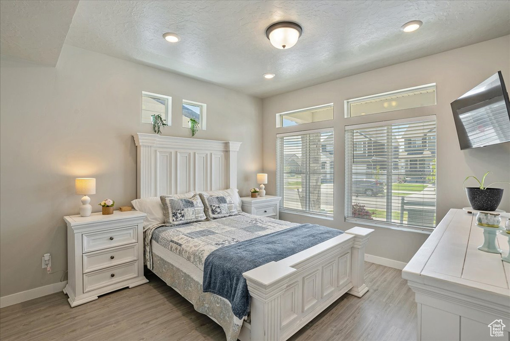 Bedroom featuring baseboards, multiple windows, light wood-style flooring, a textured ceiling, and recessed lighting
