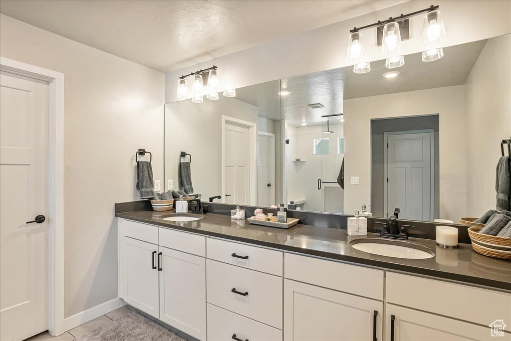 Full bath featuring double vanity, walk in shower, baseboards, and tile patterned flooring