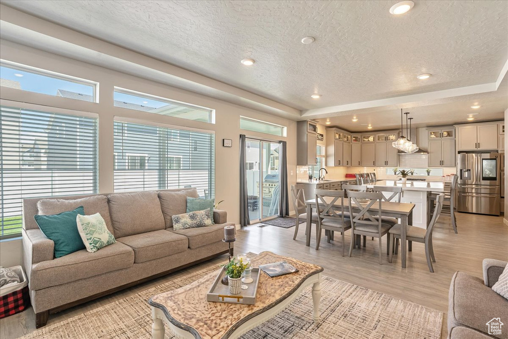 Living room featuring a textured ceiling, plenty of natural light, light wood-type flooring, recessed lighting, and a tray ceiling