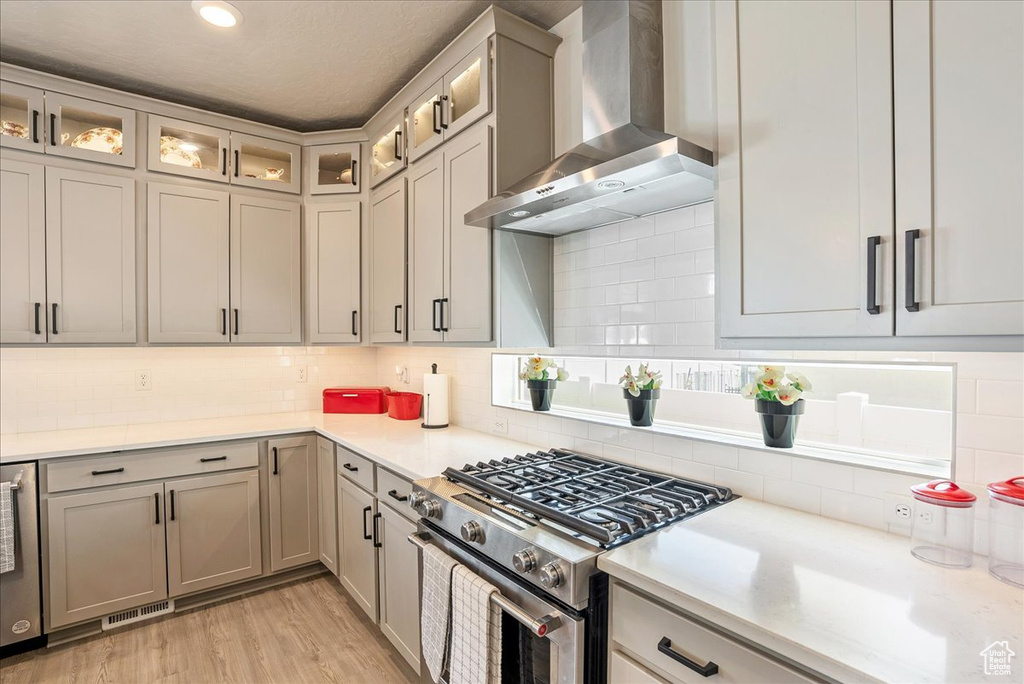 Kitchen featuring gas stove, wall chimney range hood, decorative backsplash, light countertops, and recessed lighting