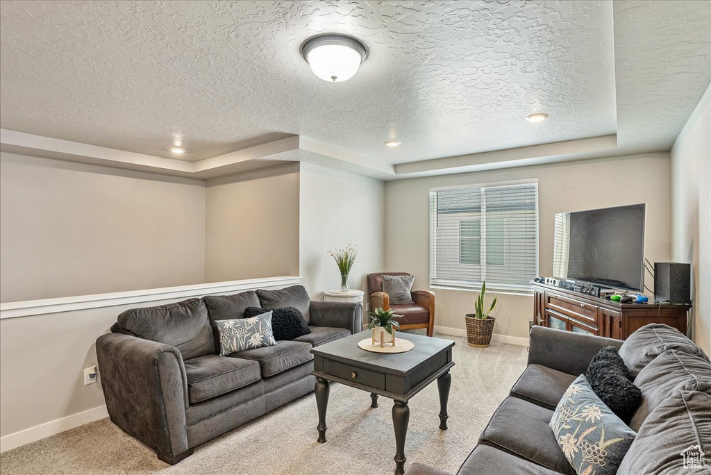 Living room with a tray ceiling, a textured ceiling, baseboards, and carpet floors