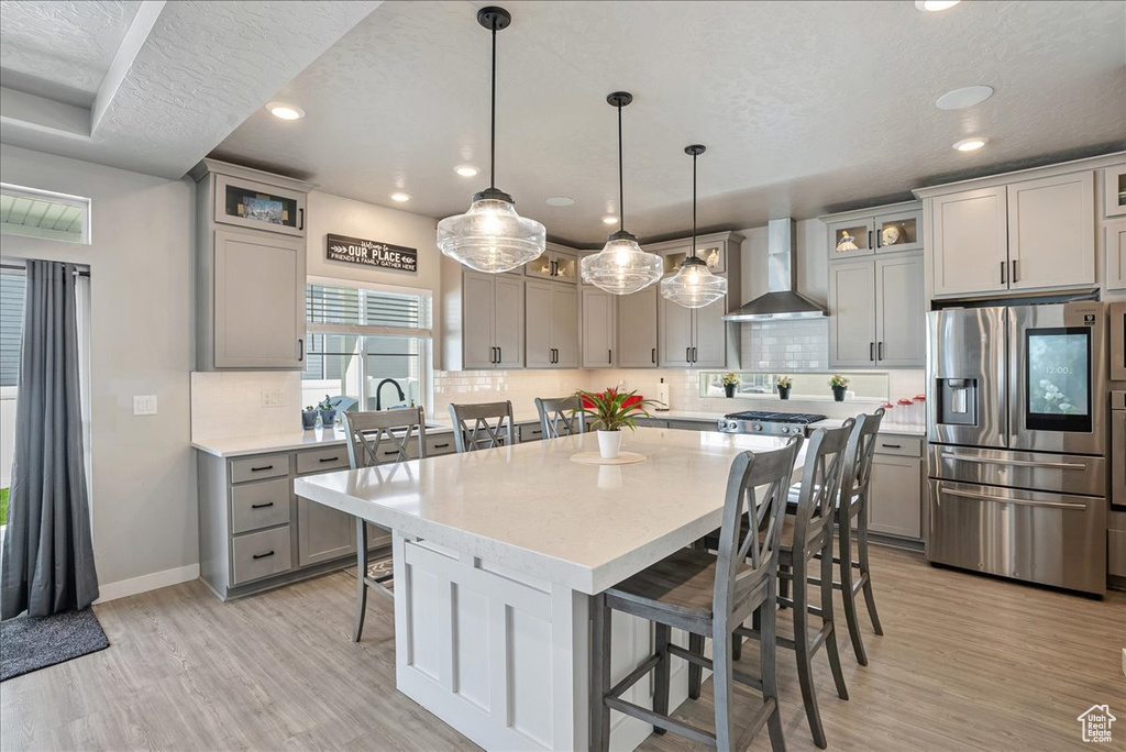 Kitchen featuring stainless steel fridge with ice dispenser, wall chimney range hood, gray cabinetry, a kitchen breakfast bar, and backsplash