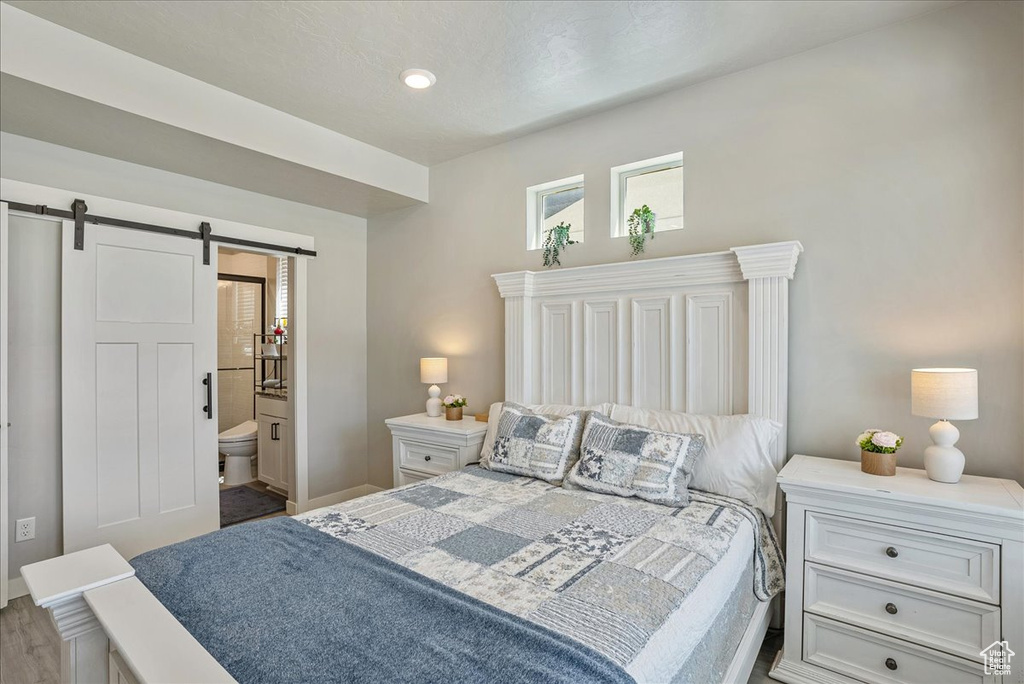 Bedroom with a barn door, baseboards, ensuite bath, and wood finished floors