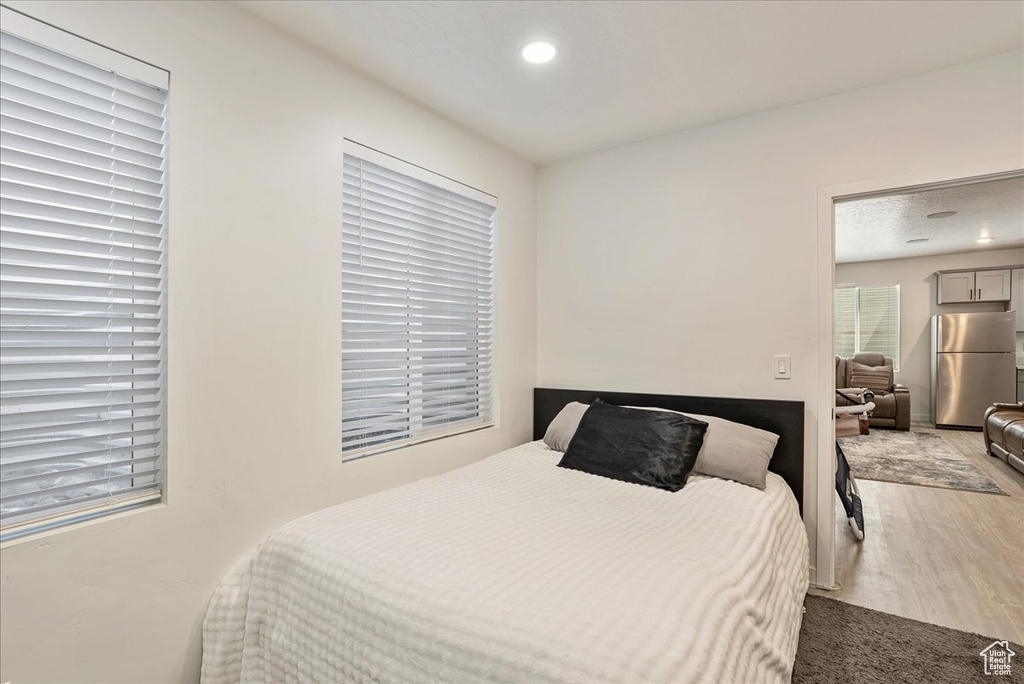 Bedroom featuring freestanding refrigerator, wood finished floors, multiple windows, and recessed lighting