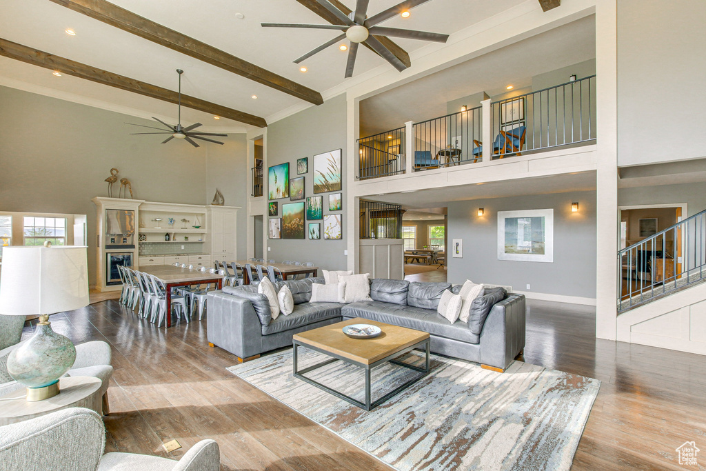 Living room featuring a ceiling fan, beamed ceiling, a high ceiling, and wood finished floors