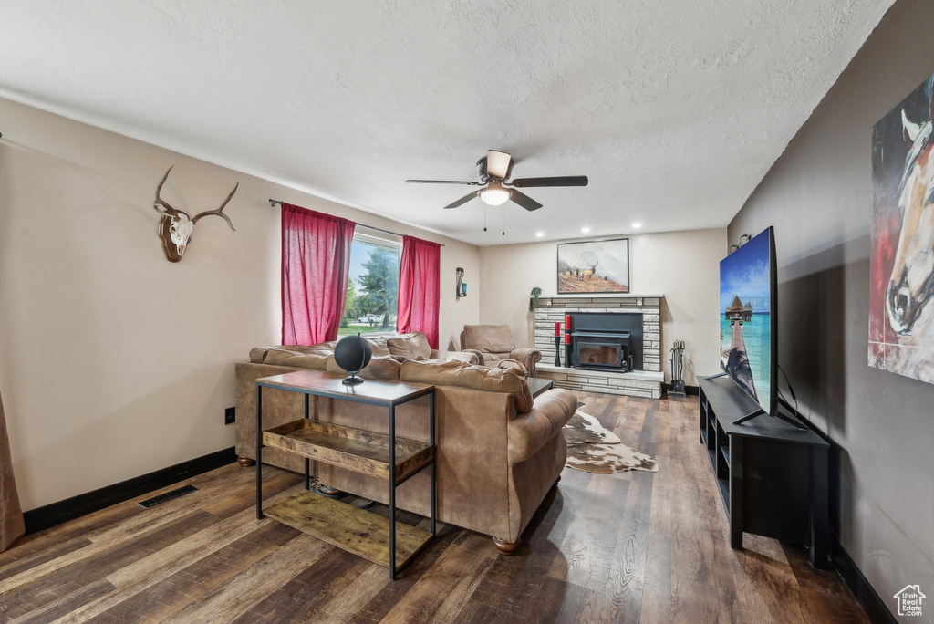 Living room featuring a ceiling fan, a fireplace, dark wood finished floors, a textured ceiling, and baseboards