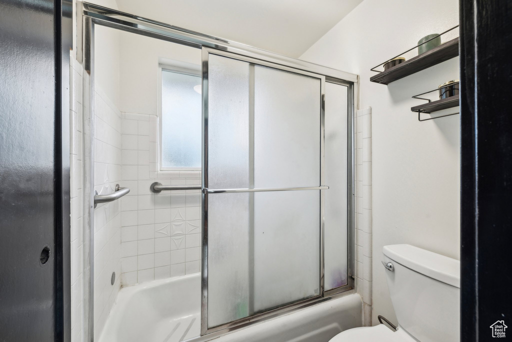 Full bathroom featuring toilet and bath / shower combo with glass door