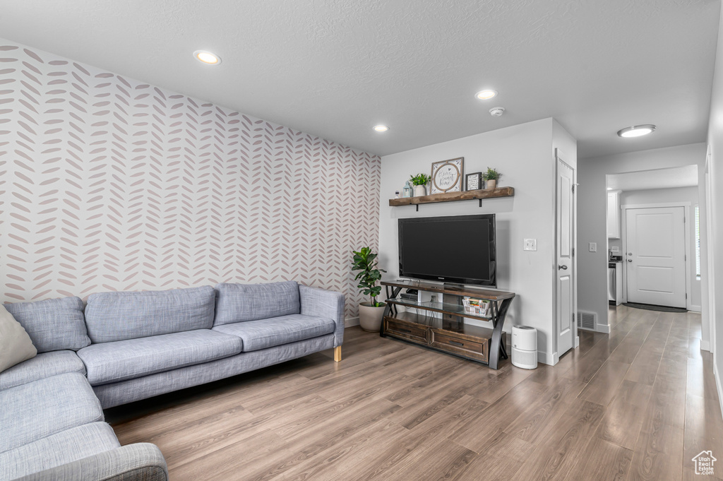 Living area featuring an accent wall, wallpapered walls, recessed lighting, baseboards, and wood finished floors