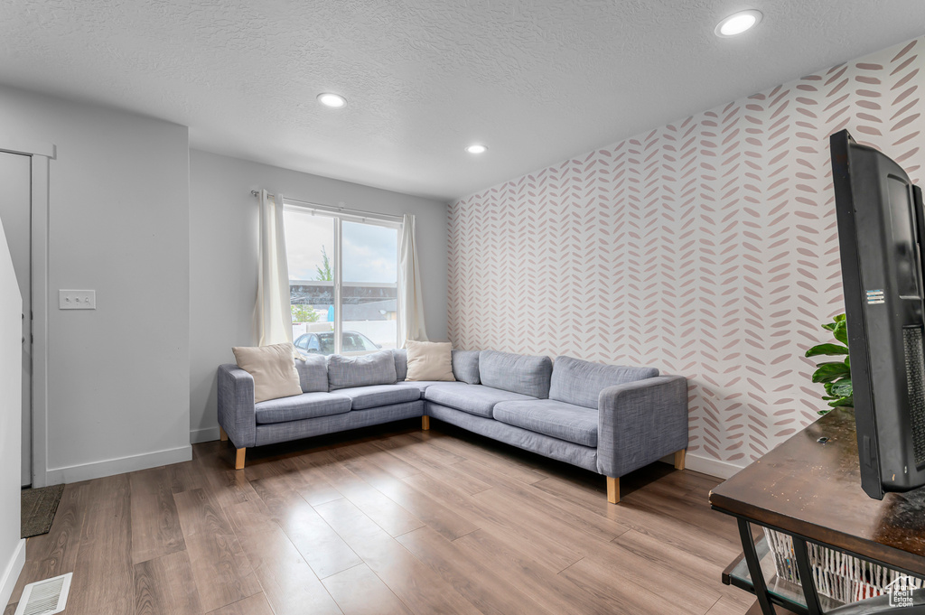 Living room featuring wallpapered walls, an accent wall, baseboards, a textured ceiling, and recessed lighting