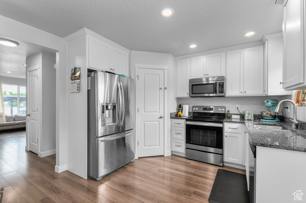 Kitchen featuring stainless steel appliances, a sink, dark wood finished floors, white cabinetry, and a textured ceiling