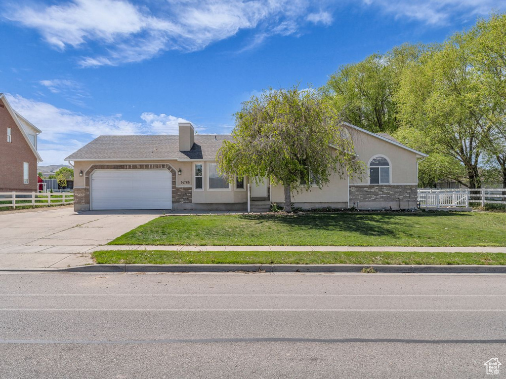 Ranch-style home with fence, an attached garage, concrete driveway, stucco siding, and a front lawn