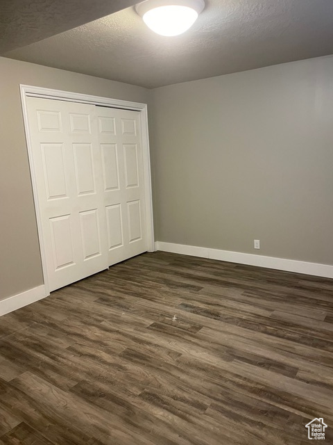 Unfurnished bedroom with a closet, dark wood finished floors, baseboards, and a textured ceiling